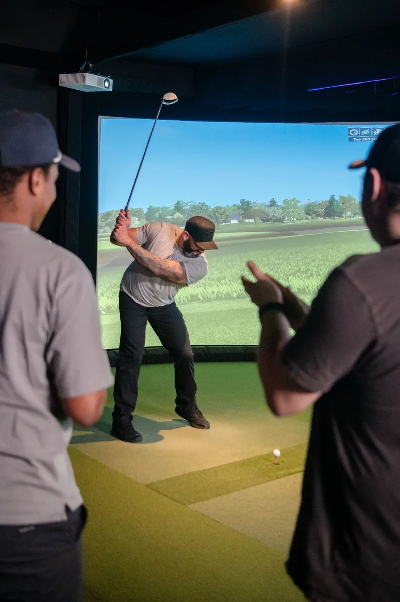 A group of friends watching one golfer take a swing on the indoor simulator at Digital Golf Fort Erie.