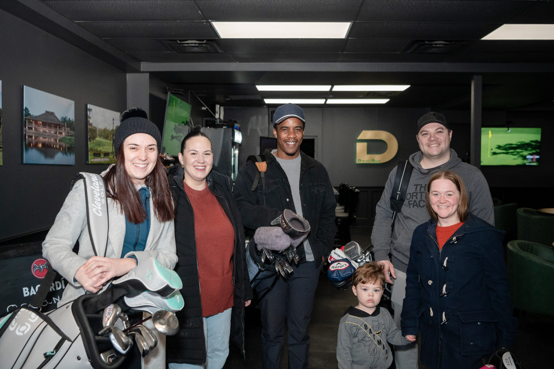 A group of customers with their golf bags inside Digital Golf Fort Erie, beside the gold Digital Golf logo.