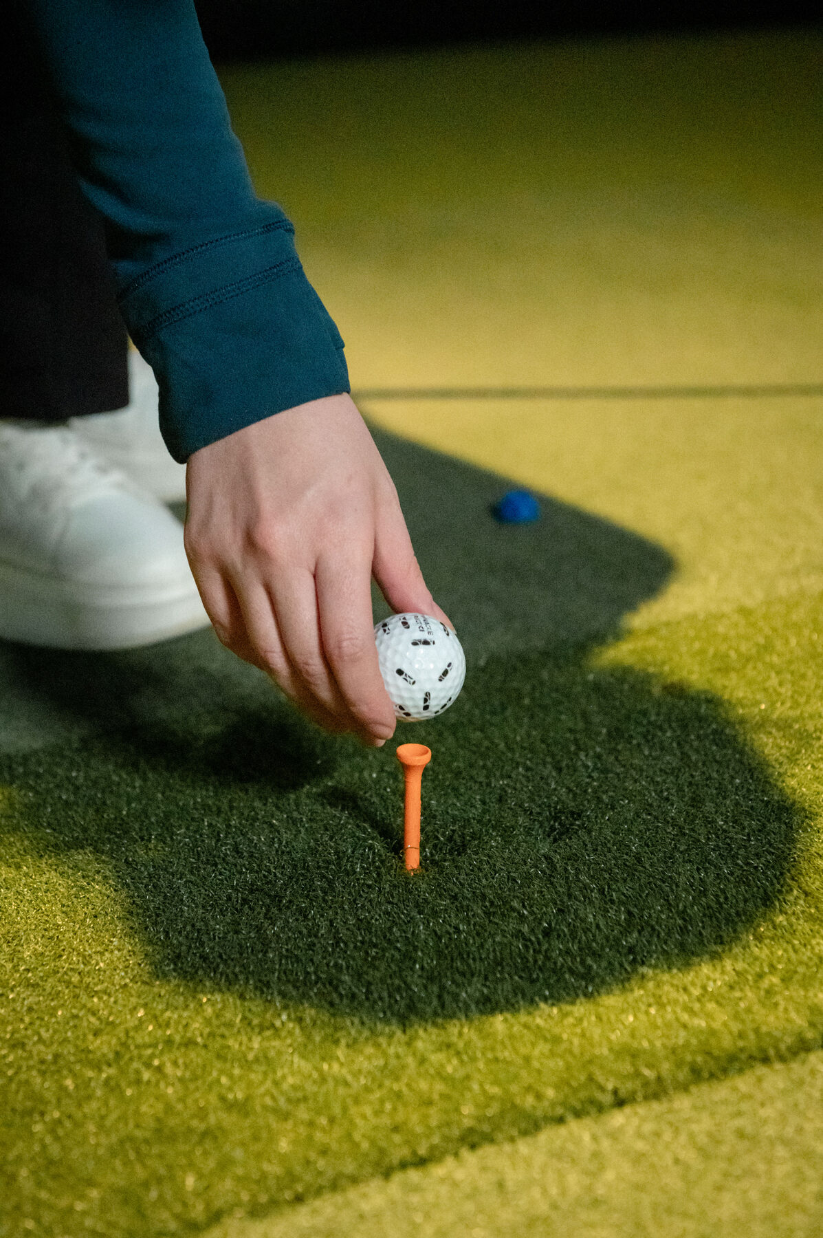Close-up of a golfer placing a ball on an orange tee on the simulator turf.