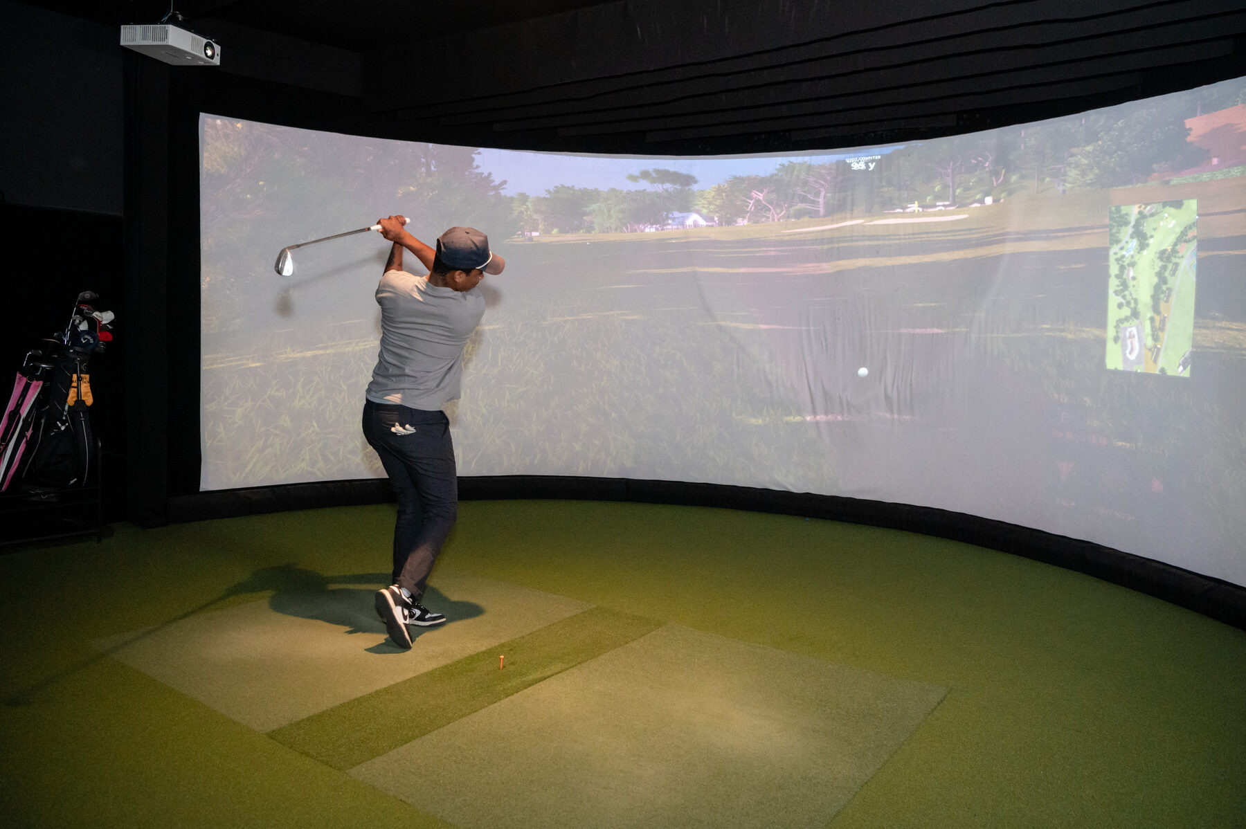 A golfer mid-swing in a simulator bay at Digital Golf Fort Erie, with a fairway projected on the screen.
