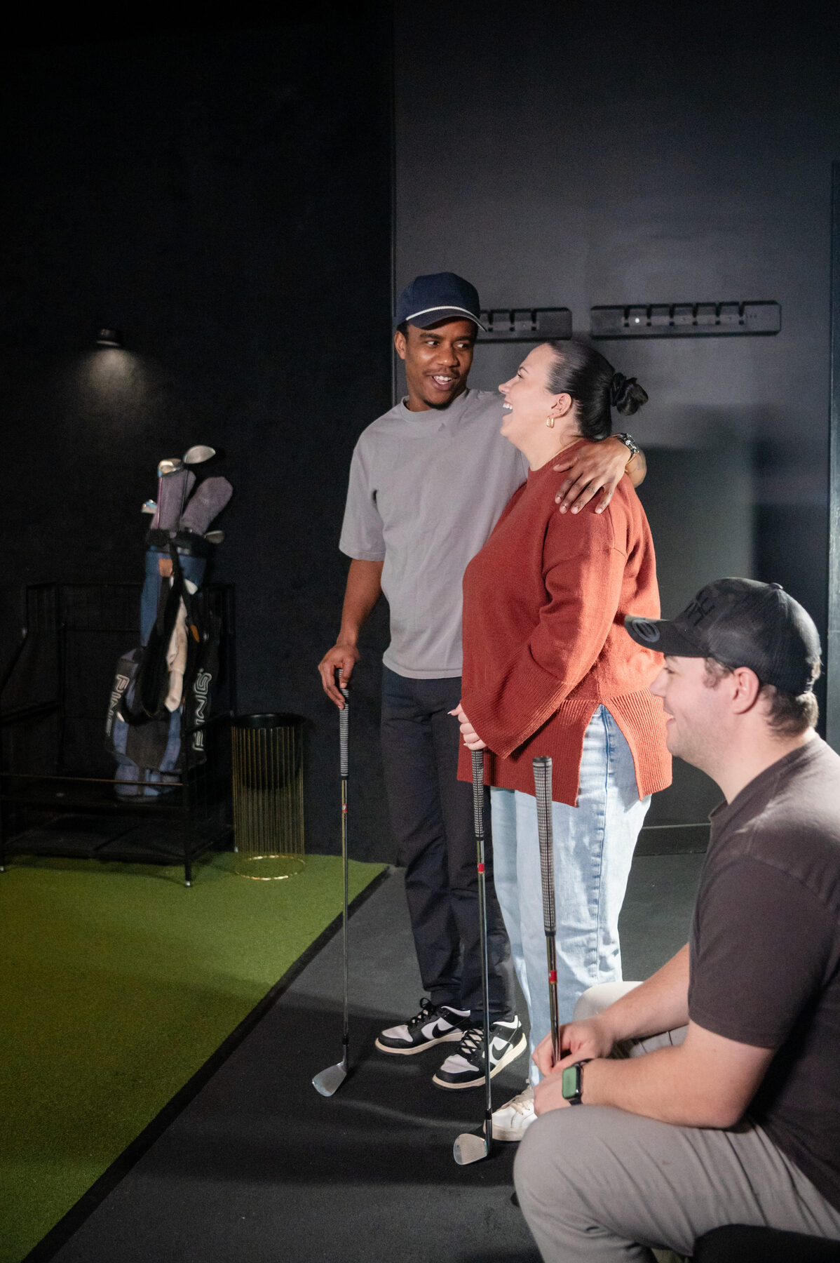 Three friends laughing together while holding clubs at Digital Golf Fort Erie.
